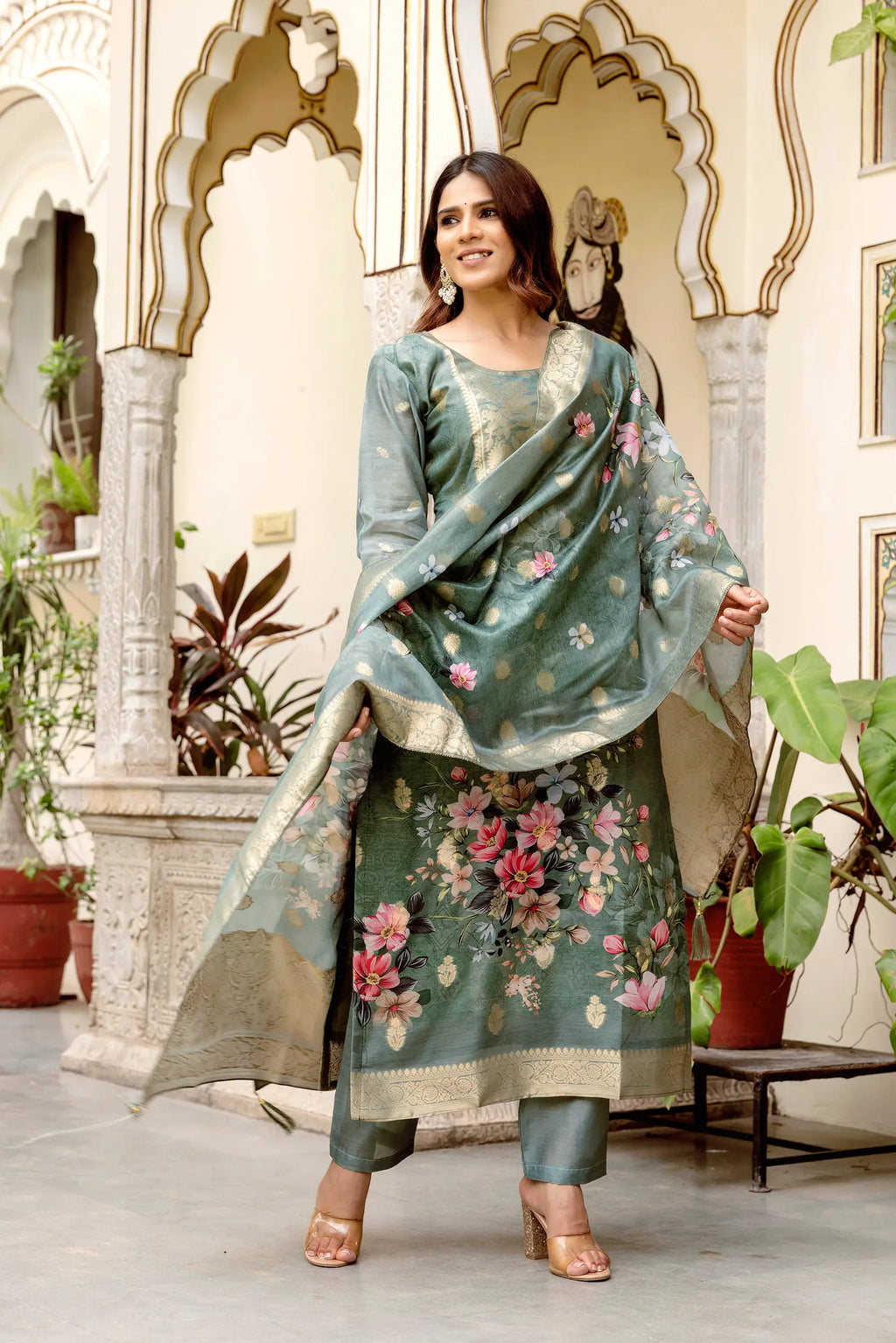 Woman in a floral traditional outfit standing in an ornate indoor setting.